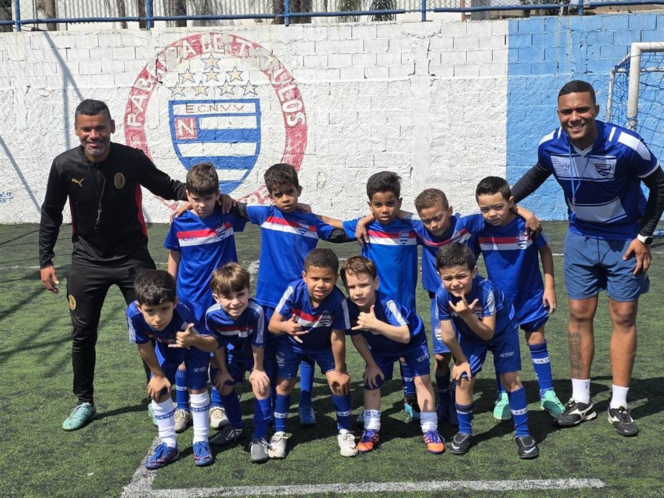 Alunos pequenos do Nacional fazendo joinha em frente ao escudo pintado no muro